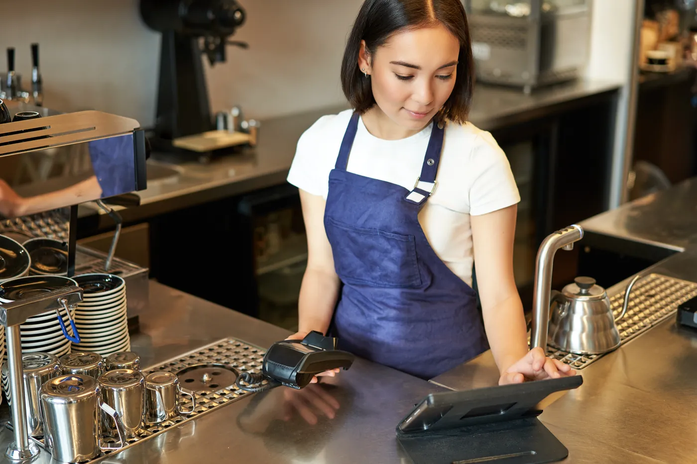 A barista at a café counter taking an order on a tablet till, with a card reader beside her
