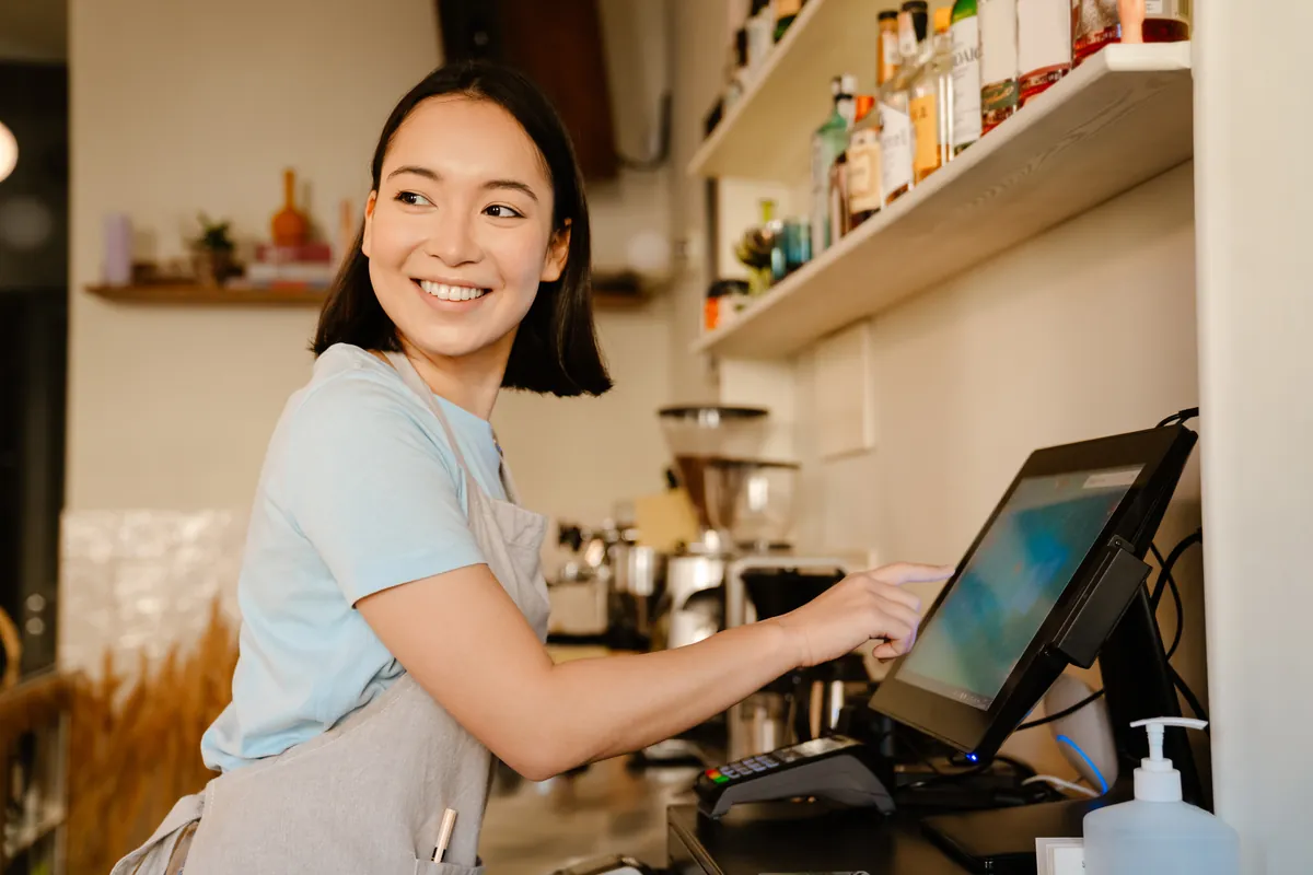 A member of staff using a touchscreen till behind a café counter